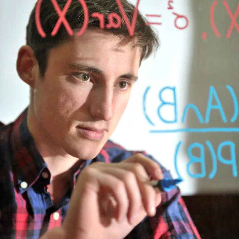 A maths student writing equations on clear glass whiteboard