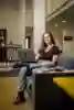 Philosophy student Mayla Singh sits on sofa with an open laptop balanced on her crossed leg