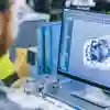 A man looks at a computer screen displaying a mechanical drawing