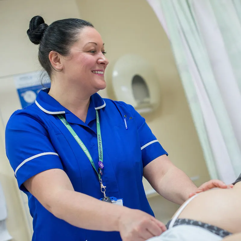 A student midwife stands next to a pregnant patient