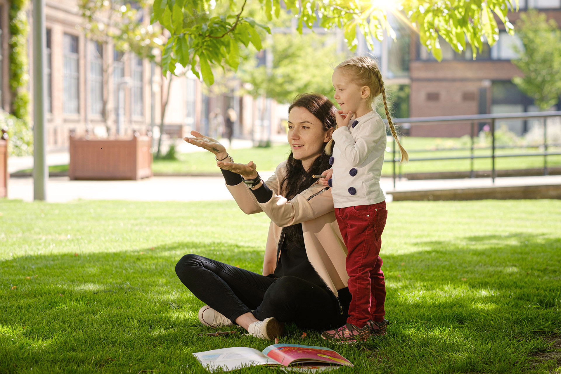 An Early Childhood Studies student sitting on outside on the grass and interacting with a child