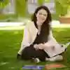 An early childhood studies student sat on the grass reading a book on a sunny day