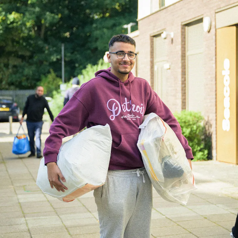 A male student stands with bags of items under his arms in the process of moving in to Westfield Court