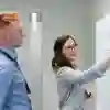 Two office workers writing on a whiteboard during a meeting
