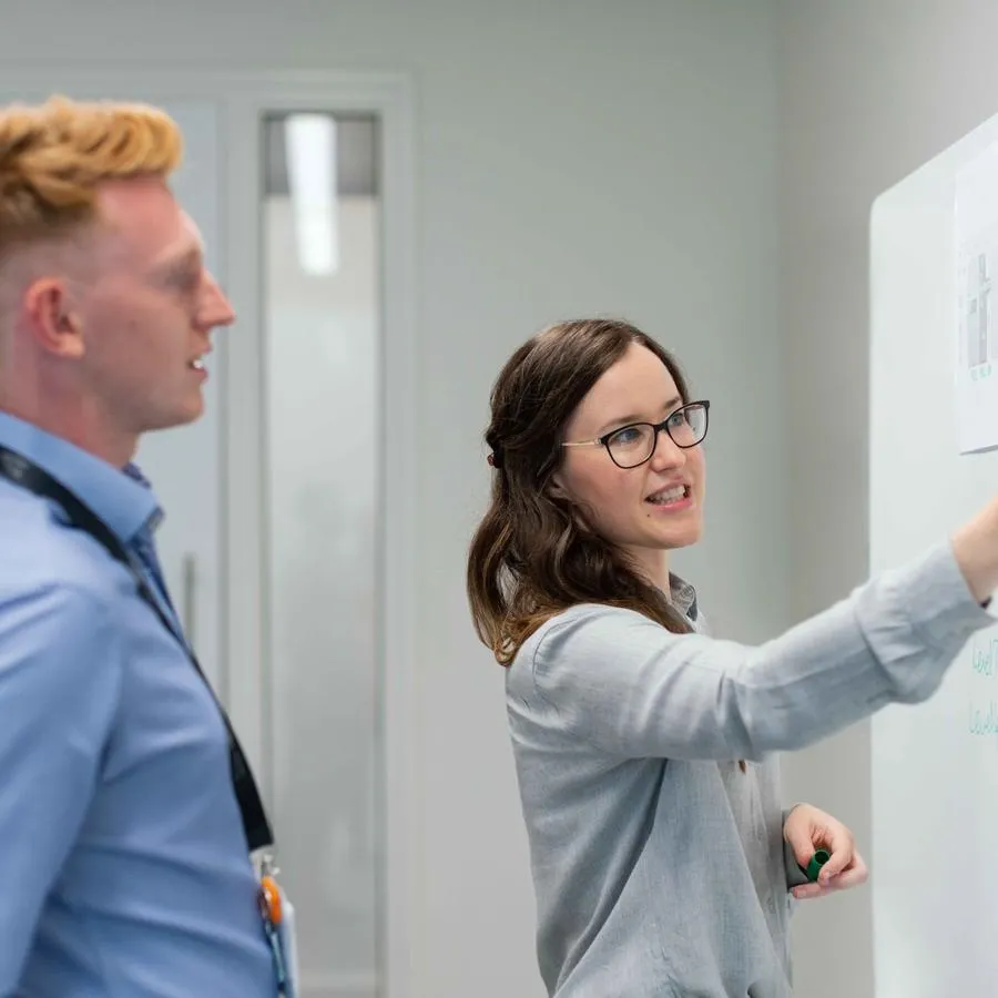Two office workers writing on a whiteboard during a meeting