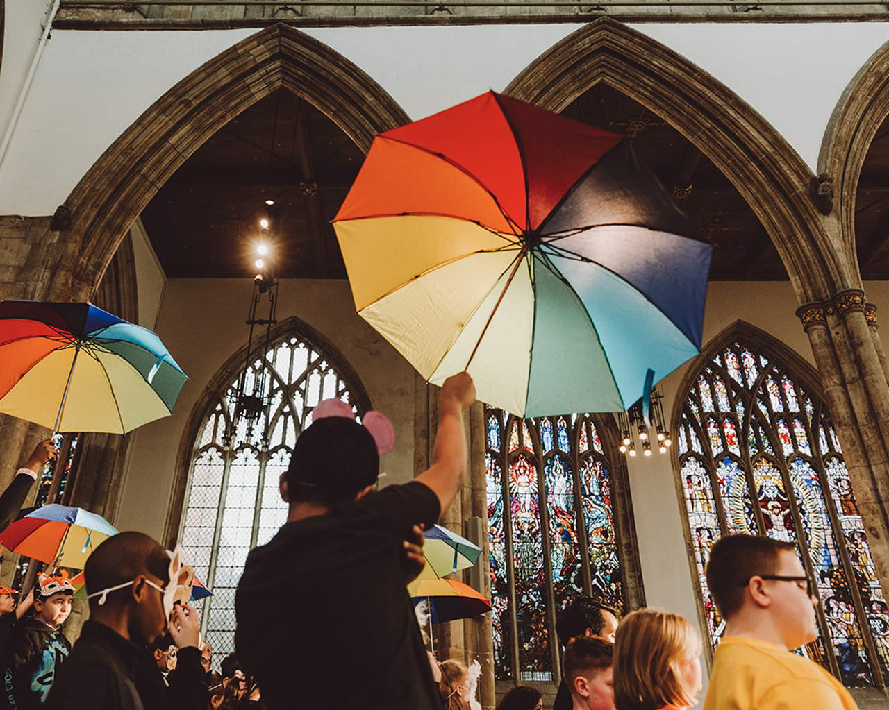 Children walk through Hull Minster wearing masks and holding rainbow umbrellas
