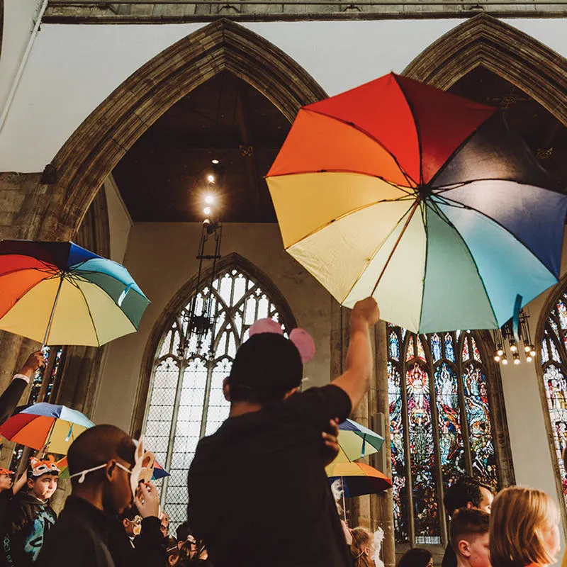 Children walk through Hull Minster wearing masks and holding rainbow umbrellas