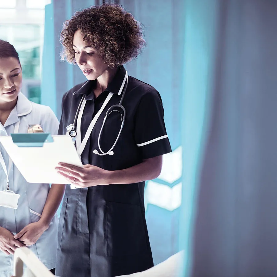 Two nurses in a hospital setting looking at notes on a clipboard