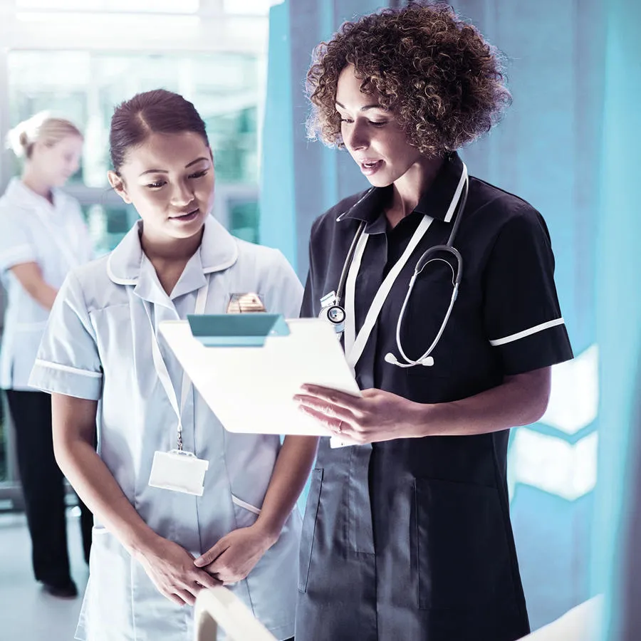 Two nurses in a hospital setting looking at notes on a clipboard