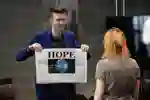 A performer shows a newspaper with headline 'Hope' and image of the Earth 