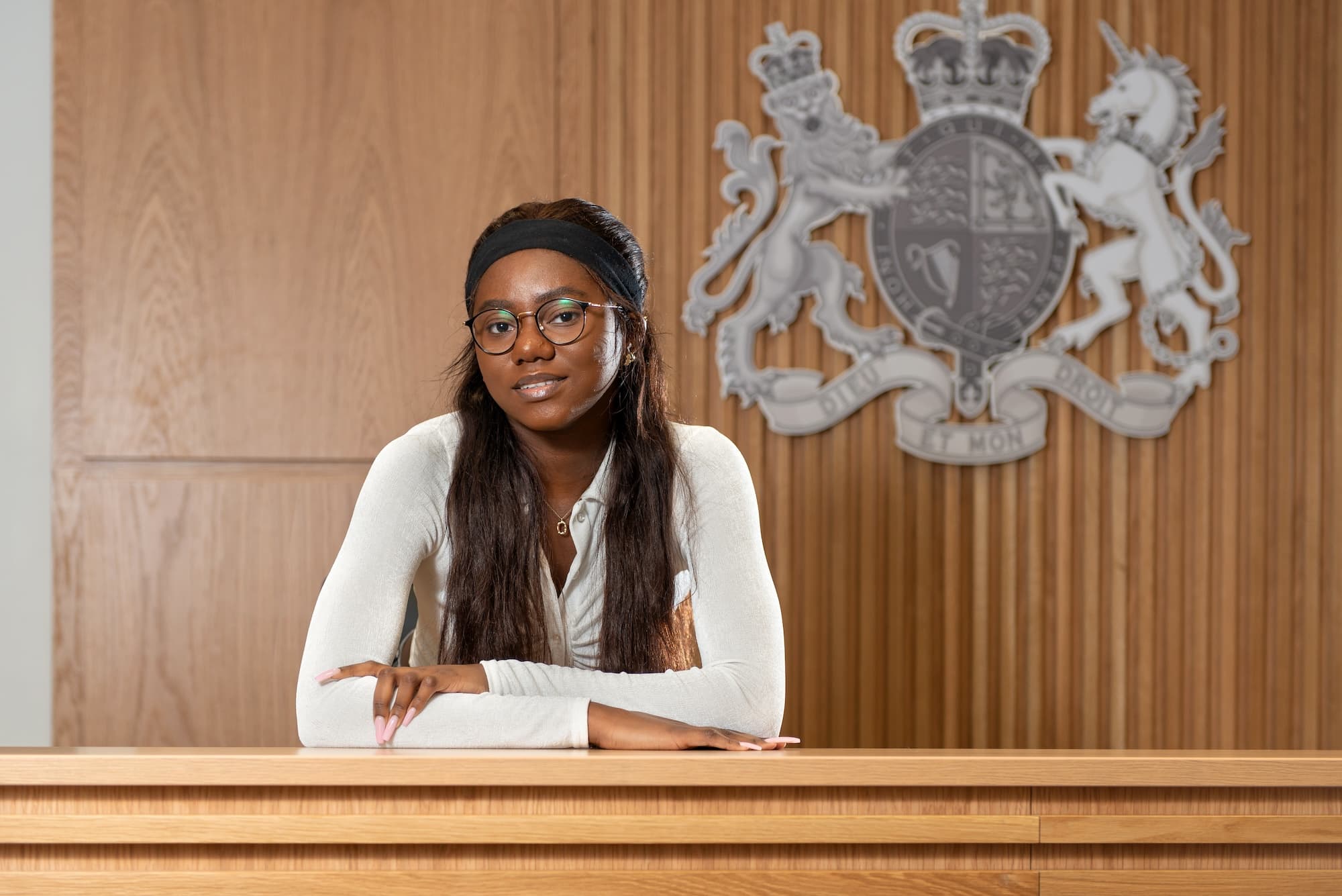 A law student poses in front of the UK royal coat of arms in a mock courtroom