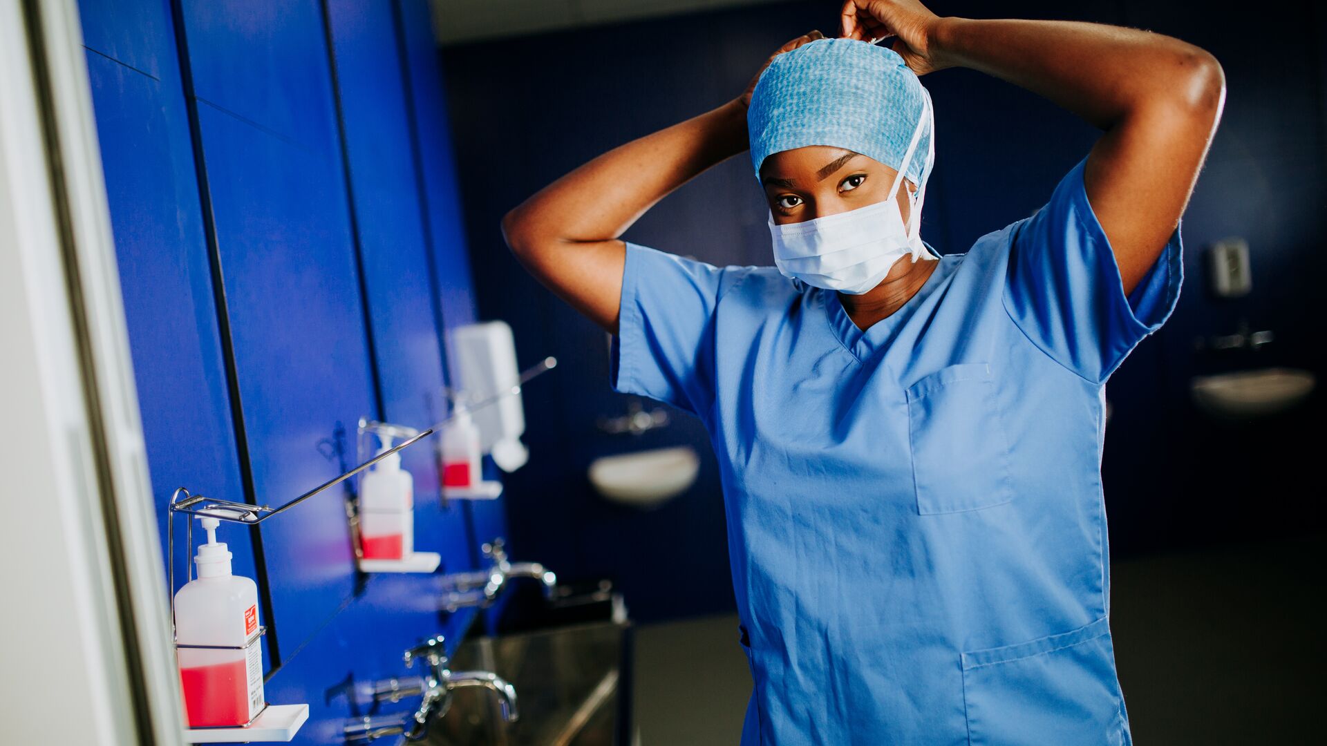 A female student in surgical scrubs ties a mask around her face