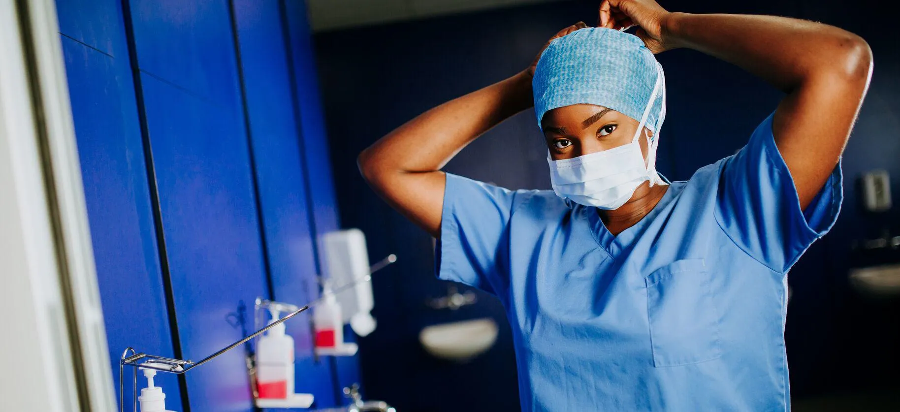 A female student in surgical scrubs ties a mask around her face