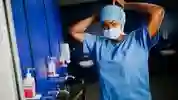 A female student in surgical scrubs ties a mask around her face