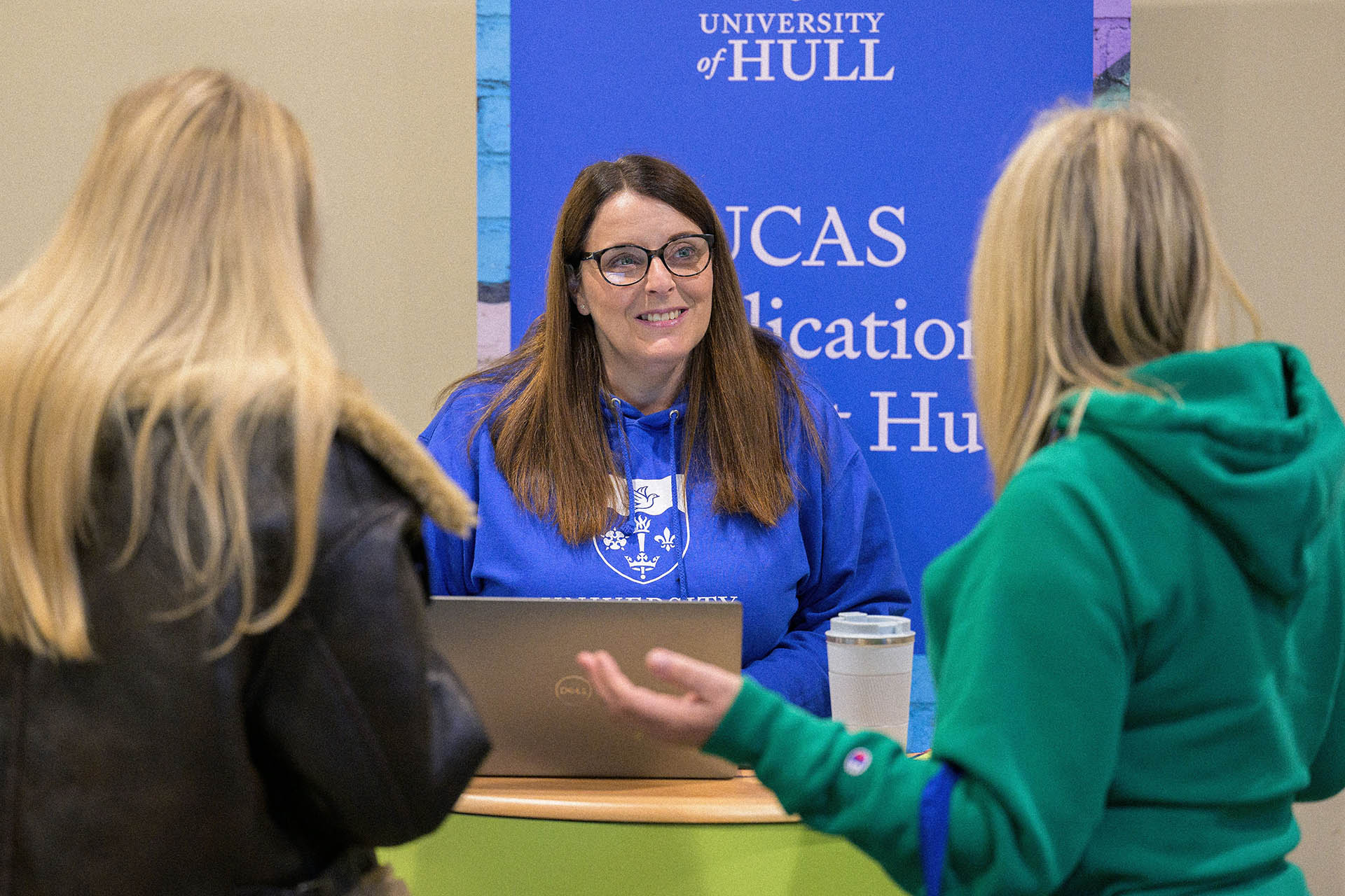 A member of staff greets prospective students on a help stand at an Open Day