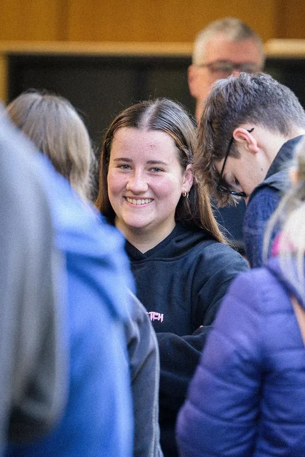 Student in crowd smiles at building.