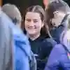 Student in crowd smiles at building.