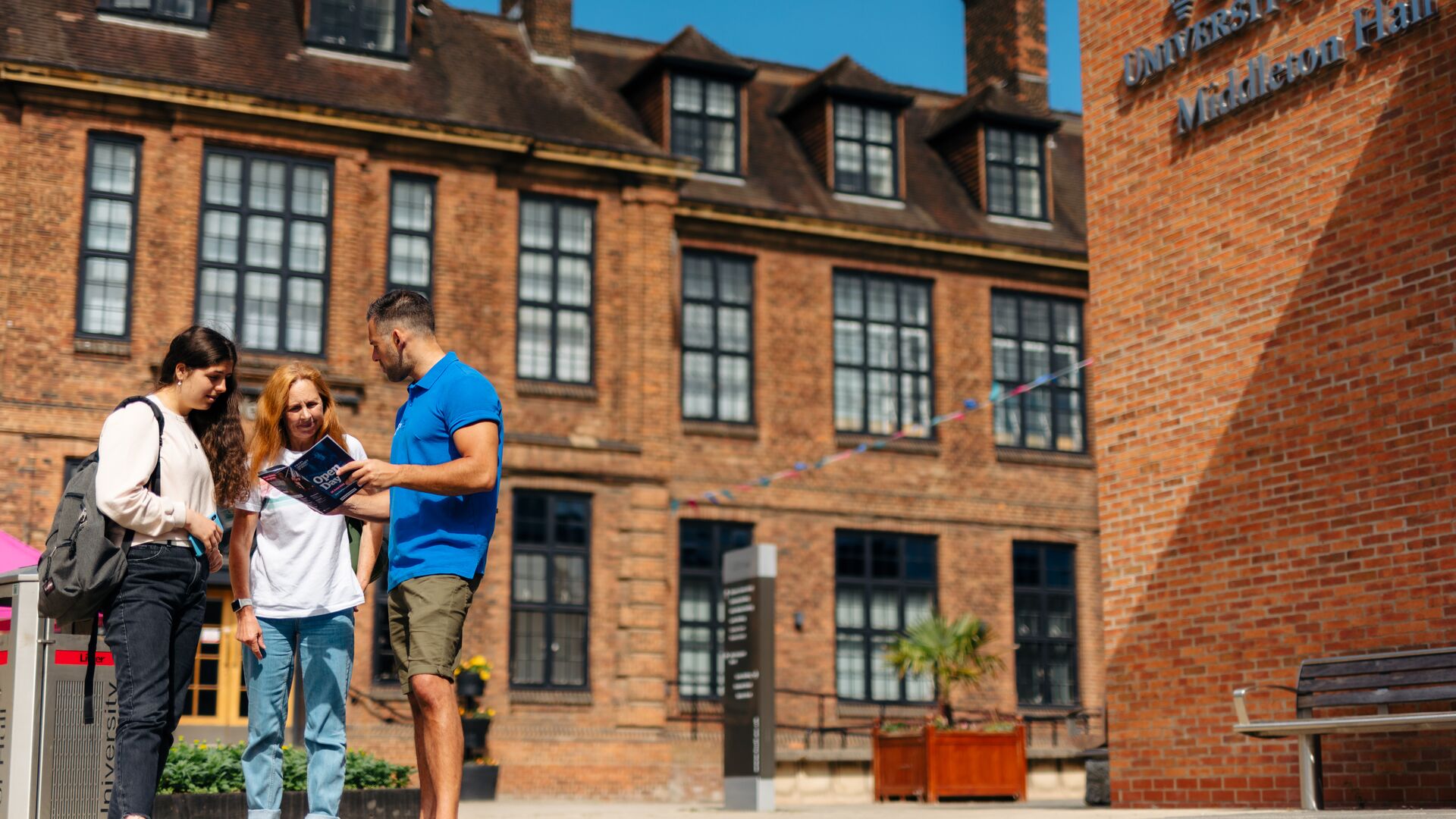 A member of staff in a bright blue polo helps two visitors at an Open Day
