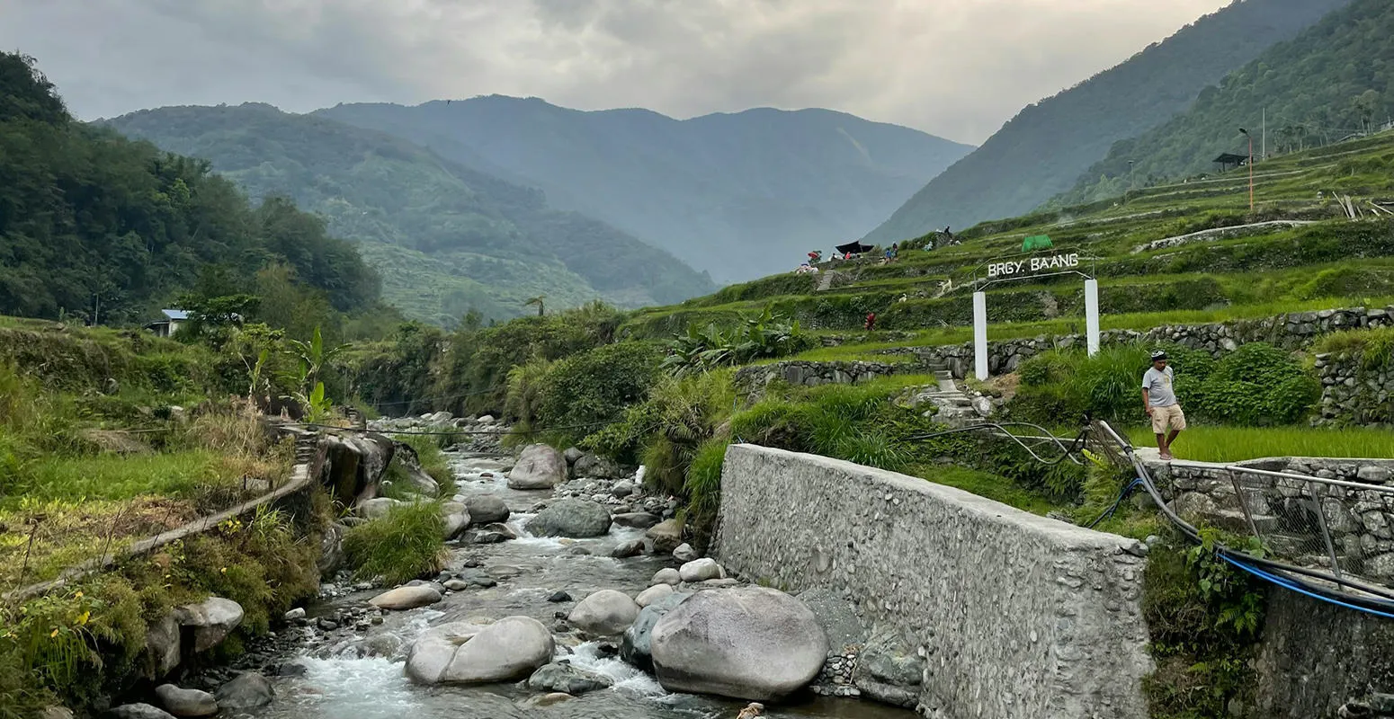 A river and water pipe run through a green valley in the Philippines