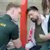 Two student paramedics practising on a patient leaning against a red post with blood on his arm