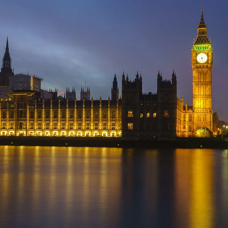 The Palace of Westminster and Big Ben lit up at night, reflected by the River Thames.