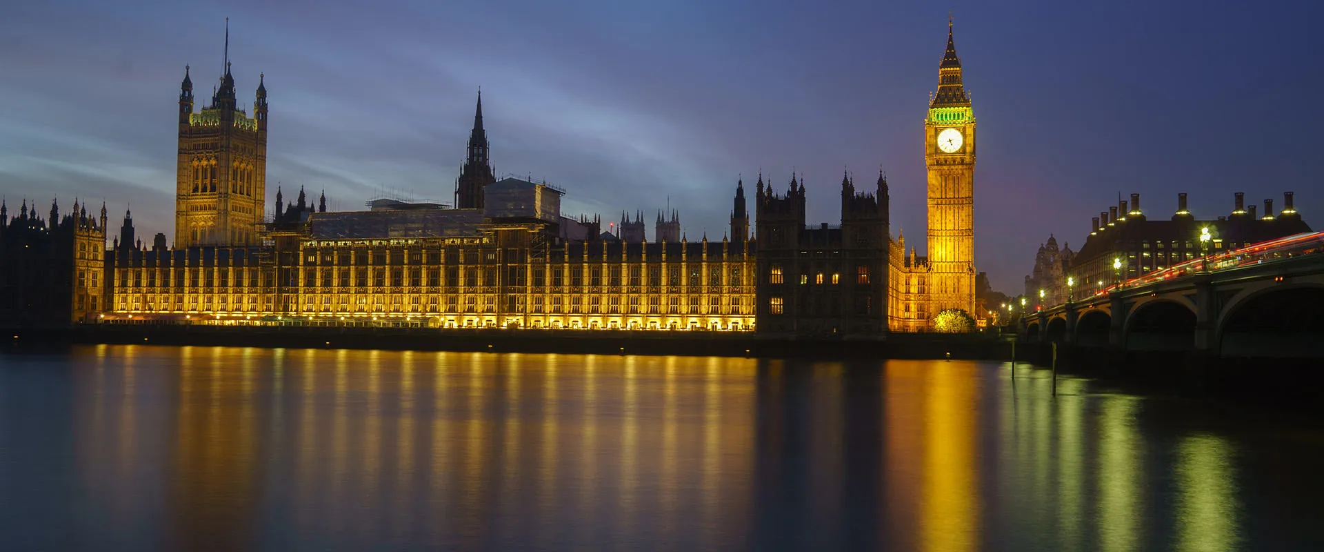 The Palace of Westminster and Big Ben lit up at night, reflected by the River Thames.