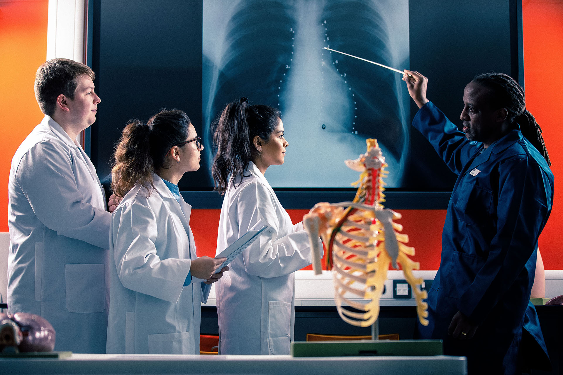 A lecturer points to an area on an x-ray in a medical lab with students writing notes