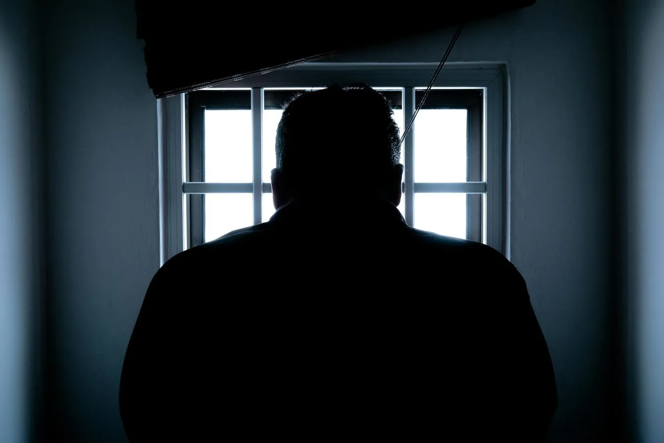 A silhouetted figure looks through a barred window