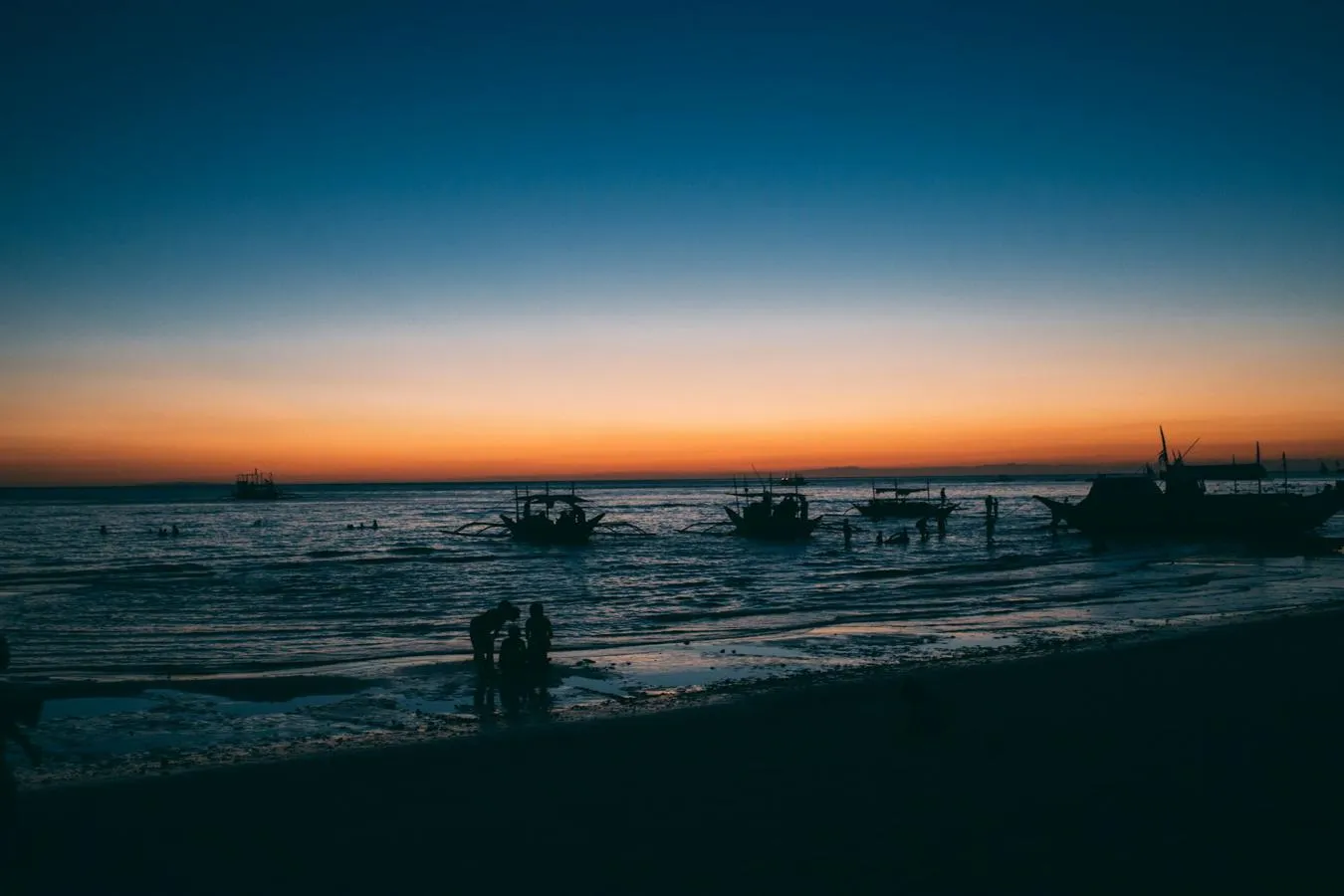 A Philippines beach scene at sunset with small boats near the shore