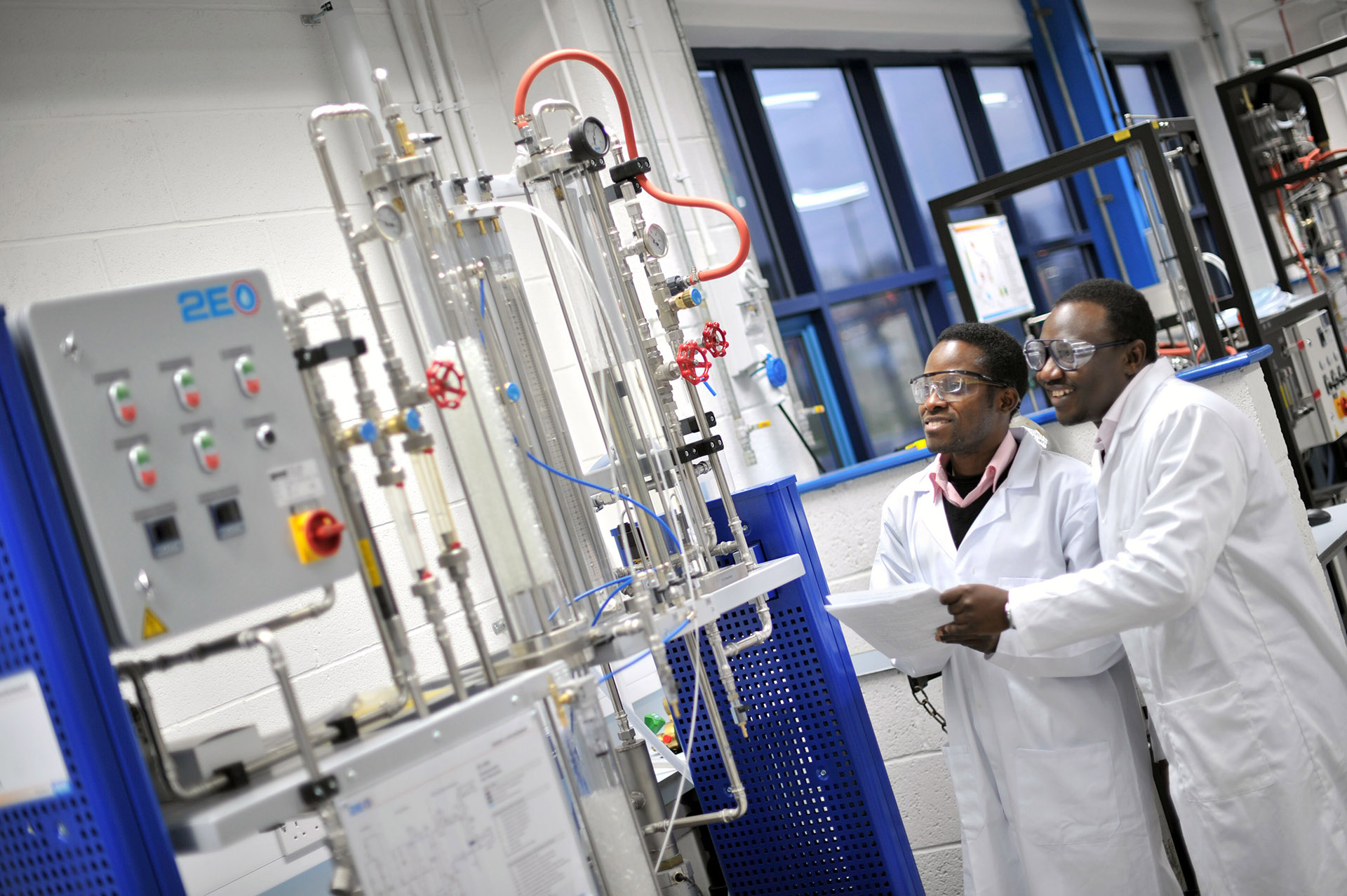 Students in white lab coats observe equipment in a chemical engineering lab