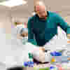 A student in a white protective suit works with a lecturer in the crime scene lab