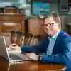 Man in suit sitting at a table with an open laptop and notebook
