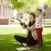 An Early Childhood Studies student sitting on outside on the grass and interacting with a child