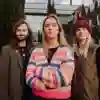 Three staff members stand confidently in front of the Business School