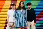 Three students standing confidently in front of rainbow coloured shutters