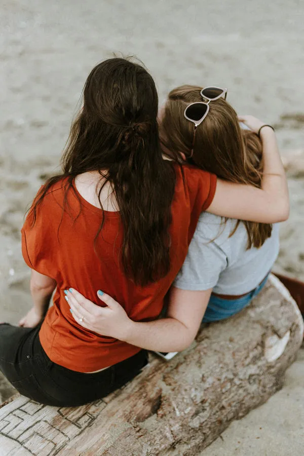older woman hugging a younger women sitting on a log on a beach