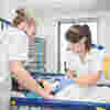 Two student nurses in white uniforms care for a young patient
