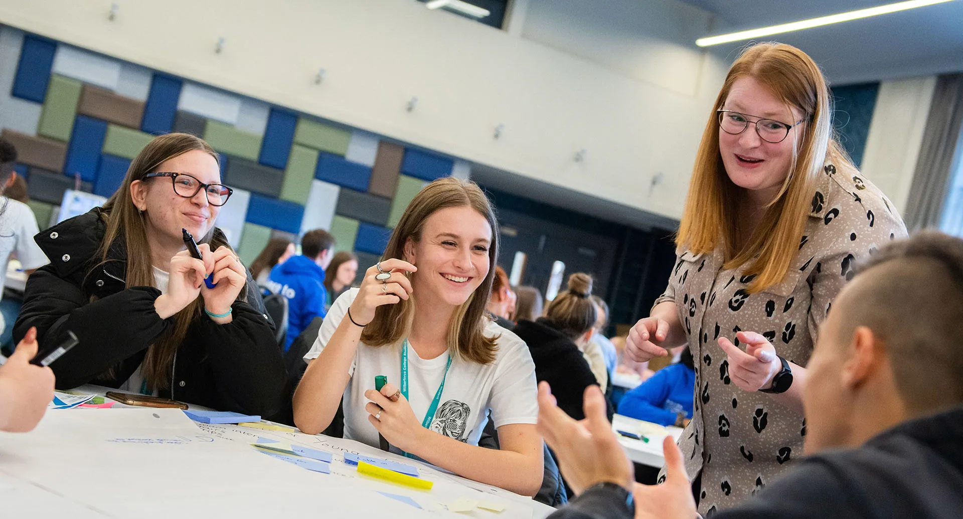 Students gather at a table with their teacher, participating in a discussion and sharing ideas in a group setting