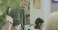Young man with glasses stands and chats to a group of older ladies in a classroom setting