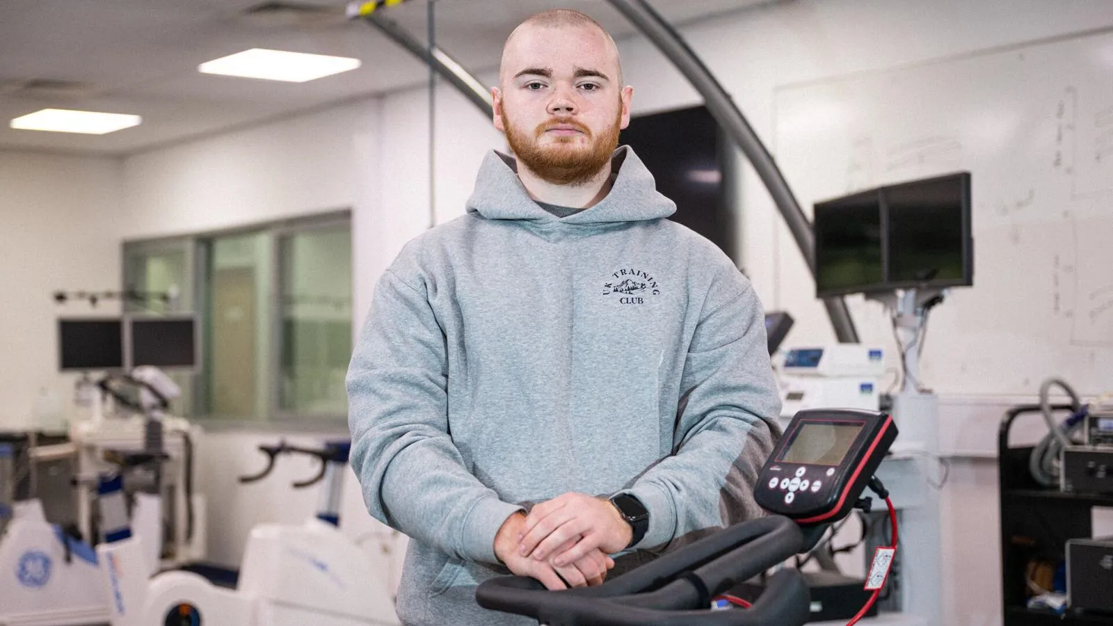 A Hull sport student wearing a grey hoody leaning against an exercise bike in a gym