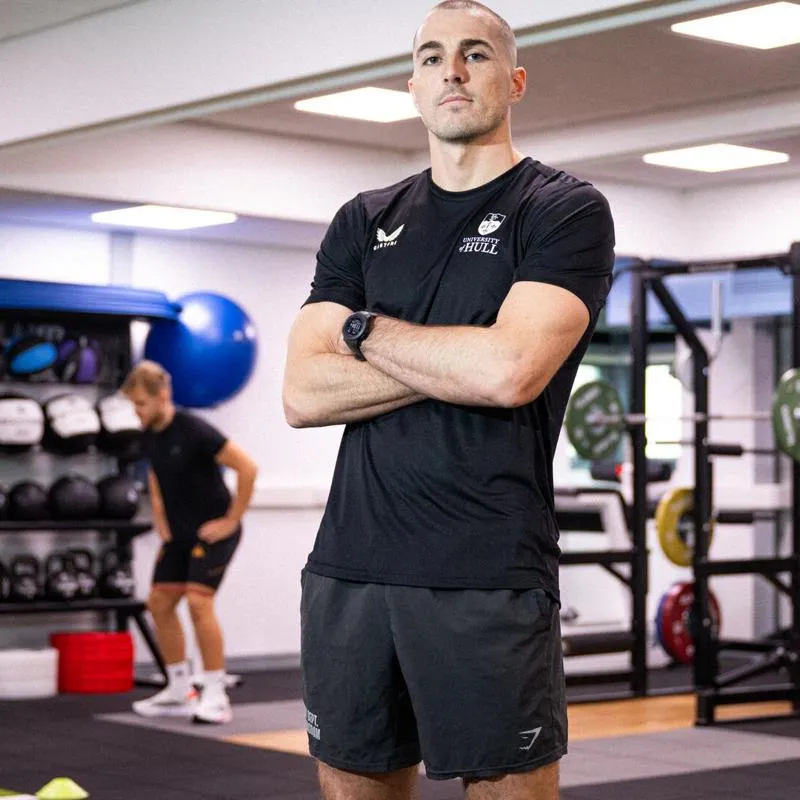 Sports student Danny Uscroft-Mould stands, arms crossed, in a gym while other users workout on equipment behind him