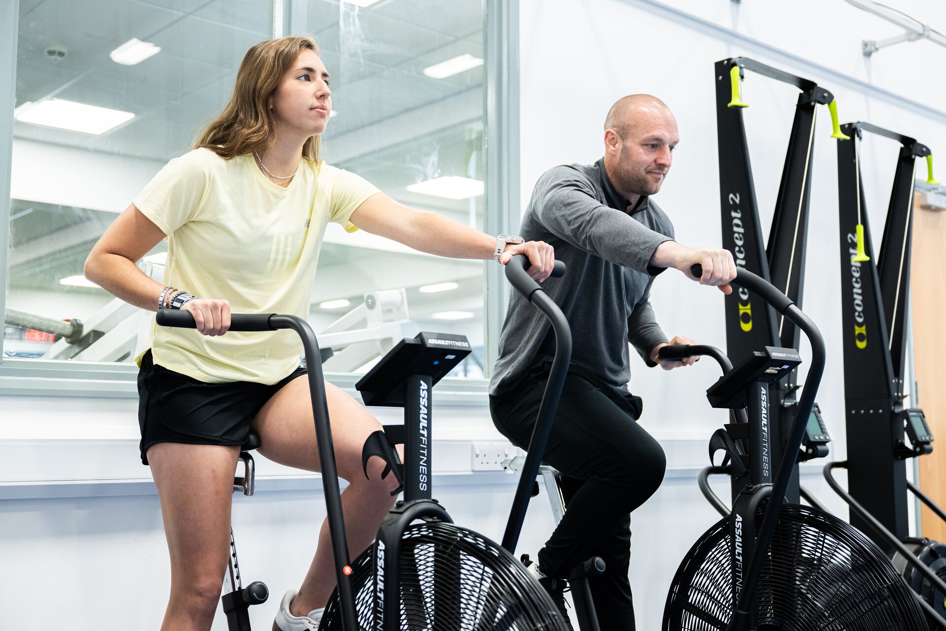 Two people exercising on stationary bikes in the Strength and Conditioning Suite on campus.