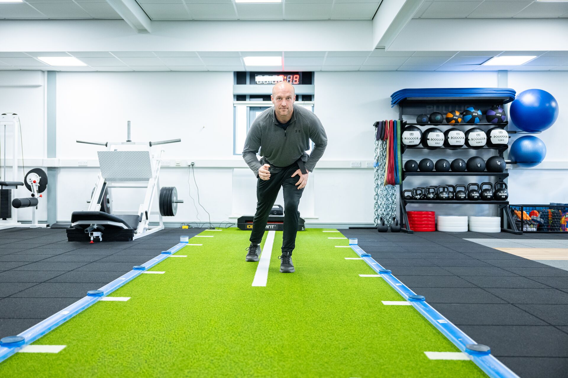 Man running or exercising on a green turf track in the Strength and Conditioning Suite.