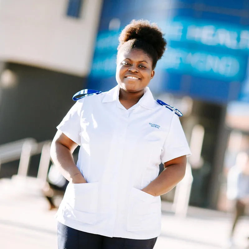 A nursing student in a white uniform stood in front of the university's medical building on campus