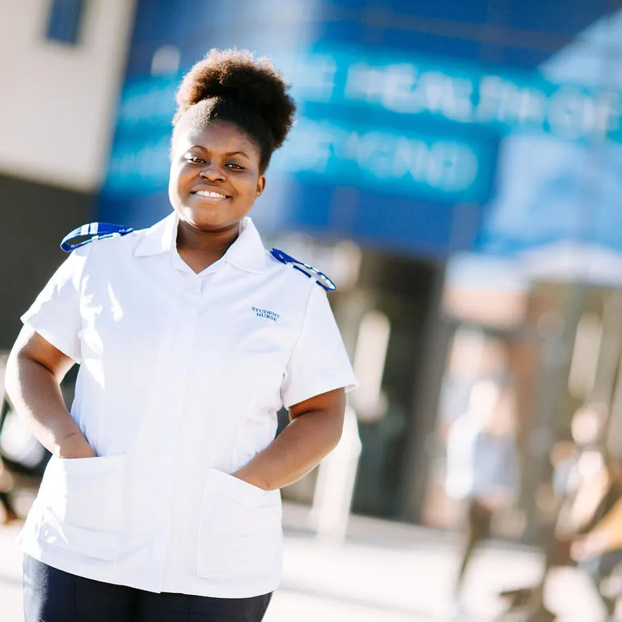 A nursing student in a white uniform stood in front of the university's medical building on campus