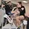 Three students in a gym, one on an exercise bike with a breathing tube on, the other two are monitoring her progress