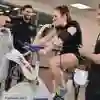 Three students in a gym, one on an exercise bike with a breathing tube on, the other two are monitoring her progress