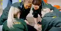 Four student paramedics in green uniforms surround a patient as part of a training exercise