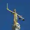 A statue of Lady Justice, blindfolded, holding a sword in one hand and scales in the other against a bright blue sky