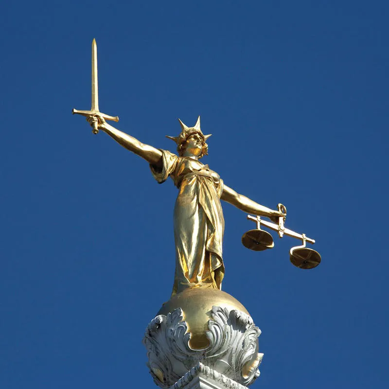 A statue of Lady Justice, blindfolded, holding a sword in one hand and scales in the other against a bright blue sky